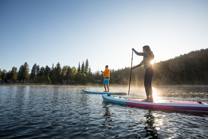 Deux personnes en planche à pagaie sur l’eau au soleil levant