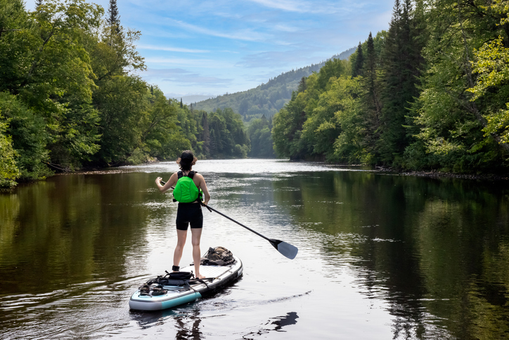 Une personne en planche à pagaie sur une rivière bordée d’arbres